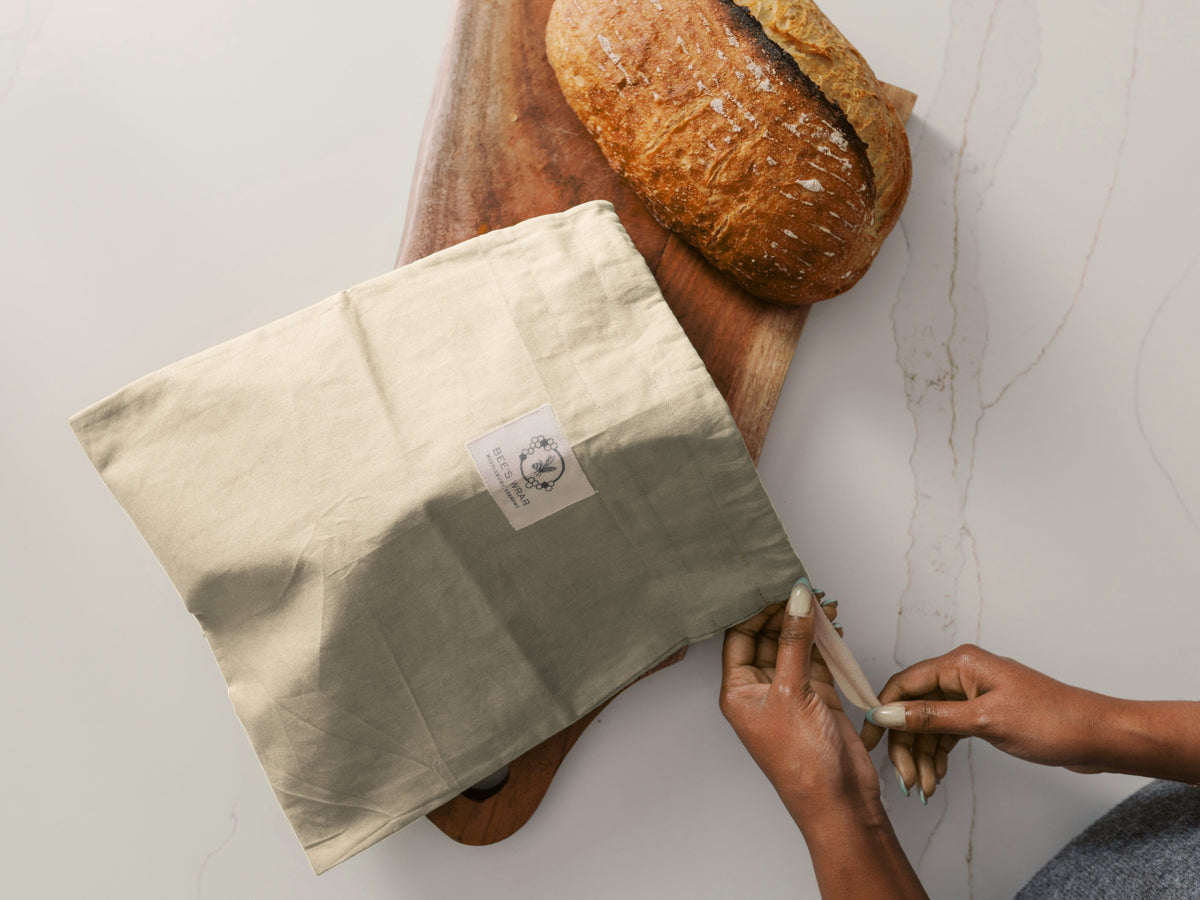 Person wrapping a loaf of bread in a Bee's Wrap Bread Bag on a white surface.