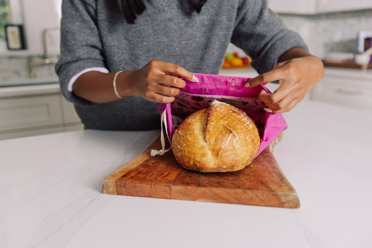 Person wrapping a loaf of bread in Meadow Magic Bread Bag on a wooden cutting board.