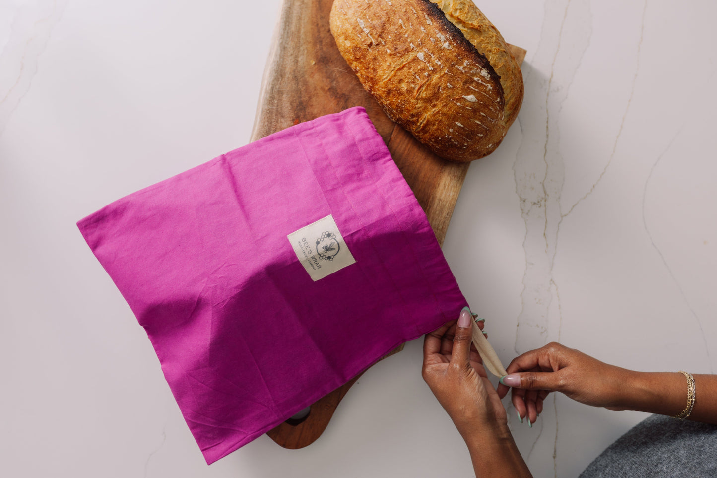 Person holding a Meadow Magic Bread Bag over a loaf of bread on a wooden board.