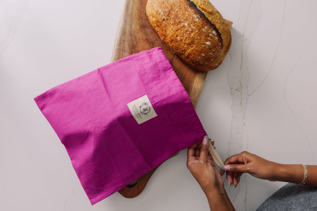 Person holding a Meadow Magic Bread Bag over a loaf of bread on a wooden board.