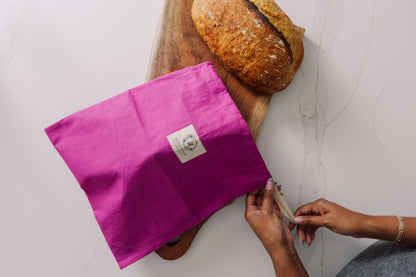 Person holding a Meadow Magic Bread Bag over a loaf of bread on a wooden board.