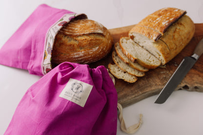 Loaves of bread in Meadow Magic Bread bags on a wooden cutting board with a knife.