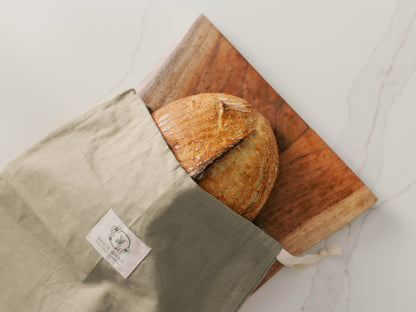Fresh loaf of bread in a Bee's Wrap Bread Bag on a cutting board.